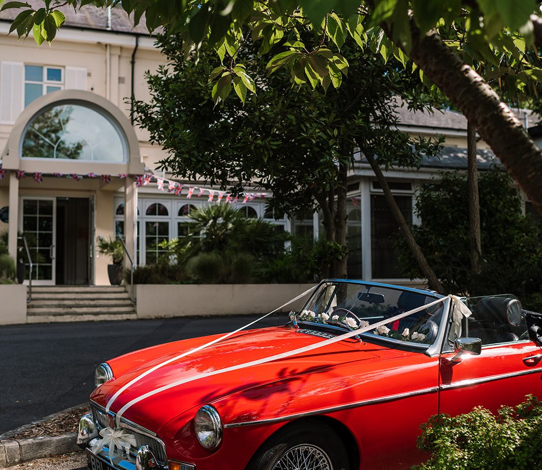 Red car with wedding ribbon in front of a building in the New Forest