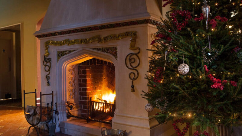 Cosy Christmas fireplace at Burley Manor, complete with roaring fire, twinkling fairy lights, and traditional festive décor—capturing the warmth and charm of a New Forest winter retreat