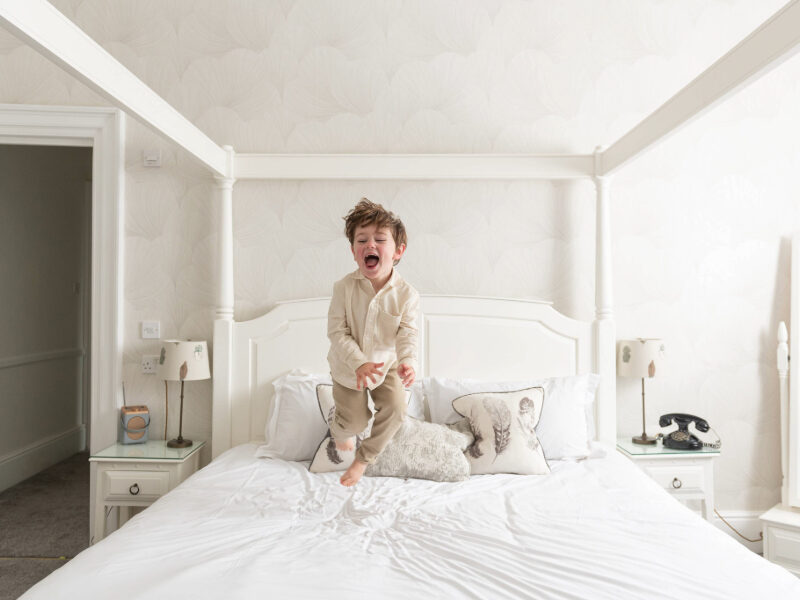A child joyfully bouncing on a hotel bed during a family stay in the New Forest, capturing the excitement and fun of a countryside getaway for families in a comfortable, welcoming hotel room.